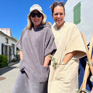 Deux femmes souriantes avec lunettes de soleil en poncho de bain graphite et sable - Atelier Dune