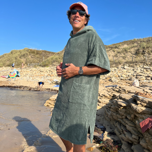 Homme souriant avec casquette debout sur la plage en poncho de bain sauge - Atelier Dune