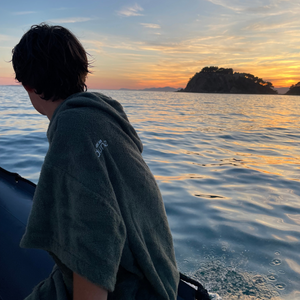 Jeune homme sur un bateau regardant coucher de soleil en poncho de bain sauge - Atelier Dune