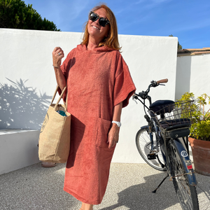 femme souriante avec un sac en paille à coté d'un vélo portant poncho de bain terracotta - Atelier Dune