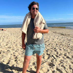 homme souriant debout sur la plage avec poncho de bain sable autour du cou - Atelier Dune