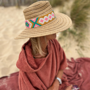 Femme avec chapeau en poncho de bain terracotta assise sur une serviette - Atelier Dune