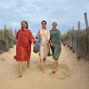 Trois filles en ponchos de bain terracotta sable et sauge marchant sur une dune - Atelier Dune