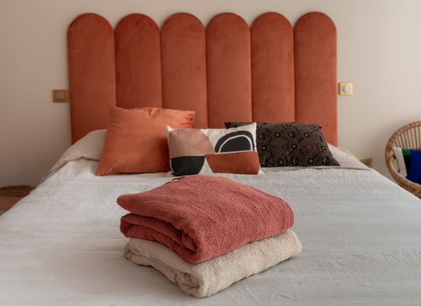 deux ponchos en coton bio terracotta et sable pliés sur un lit - Atelier Dune