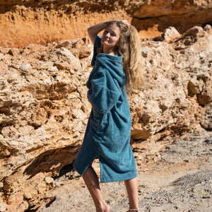 Jeune fille dans une calanque à Ibiza portant son poncho en coton bio, hyper moelleux, coloris bleu lagon Atelier Dune