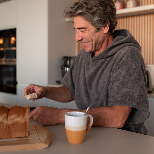 homme souriant en train de déjeuner en portat poncho de bain en coton biologique graphite - Atelier Dune