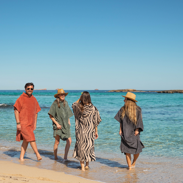 Un groupe de 4 adultes souriants marchent dans l'eau avec chcun un poncho bio zebre, terracotta, kaki sauge et graphite - Atelier Dune