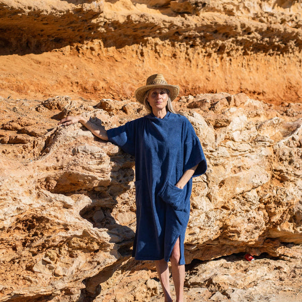 Femme avec chapeau de paille et poncho bio outremer debout contre un rocher - Atelier Dune