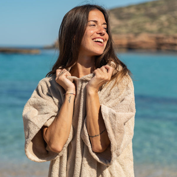 Jeune fille souriant au soleil devant la mer en poncho bio sable - Atelier Dune