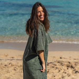 Young girl smiling at the sea in a khaki organic sage poncho. Atelier Dune