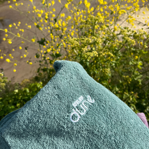 poncho de bain céladon plié sur un vélo devant des fleurs - Atelier Dune