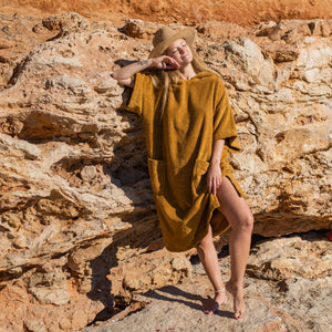 Femme souriante devant un rocher sur la plage en poncho de bain coton bio caramel - Atelier Dune