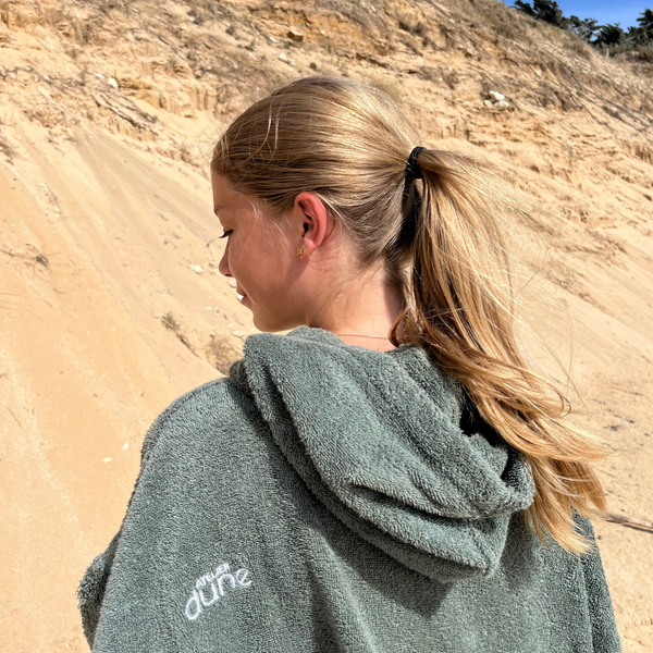 Femme de dos sur le sable portant un poncho de bain bio sauge - Atelier Dune