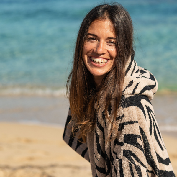 Femme souriante au bord de la plage portant un poncho en coton biologique motif zebre - Atelier Dune