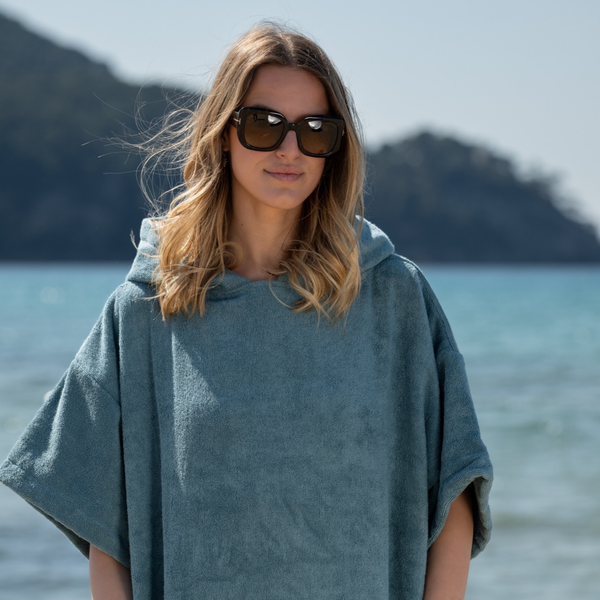 Femme souriante a la plage en poncho en coton biologique coloris bleu lagon - Atelier Dune