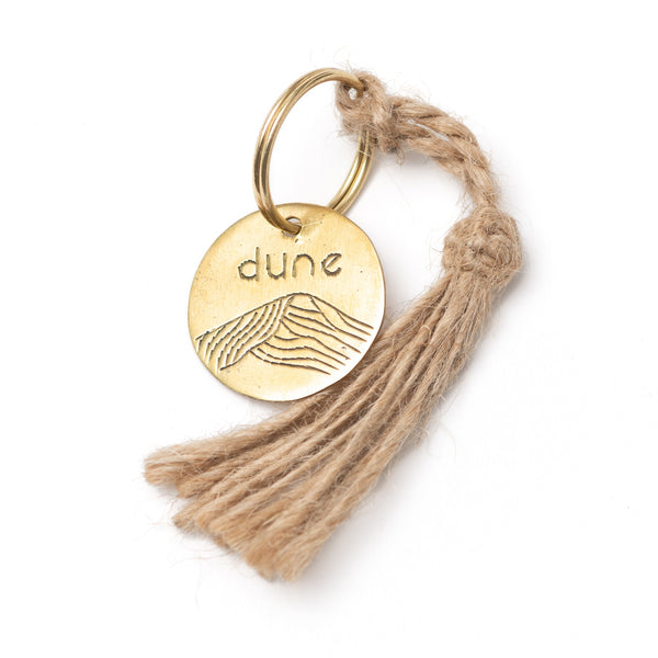 Porte-clef artisanal avec medaille gravee a la main et pompon de lin en situation lifestyle - Atelier Dune
